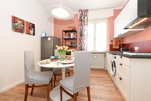 A compact kitchen with a dining area, featuring a refrigerator, microwave, and a washing machine. - Garden Apartment Bardolino - Coral Apartment (Bardolino)
