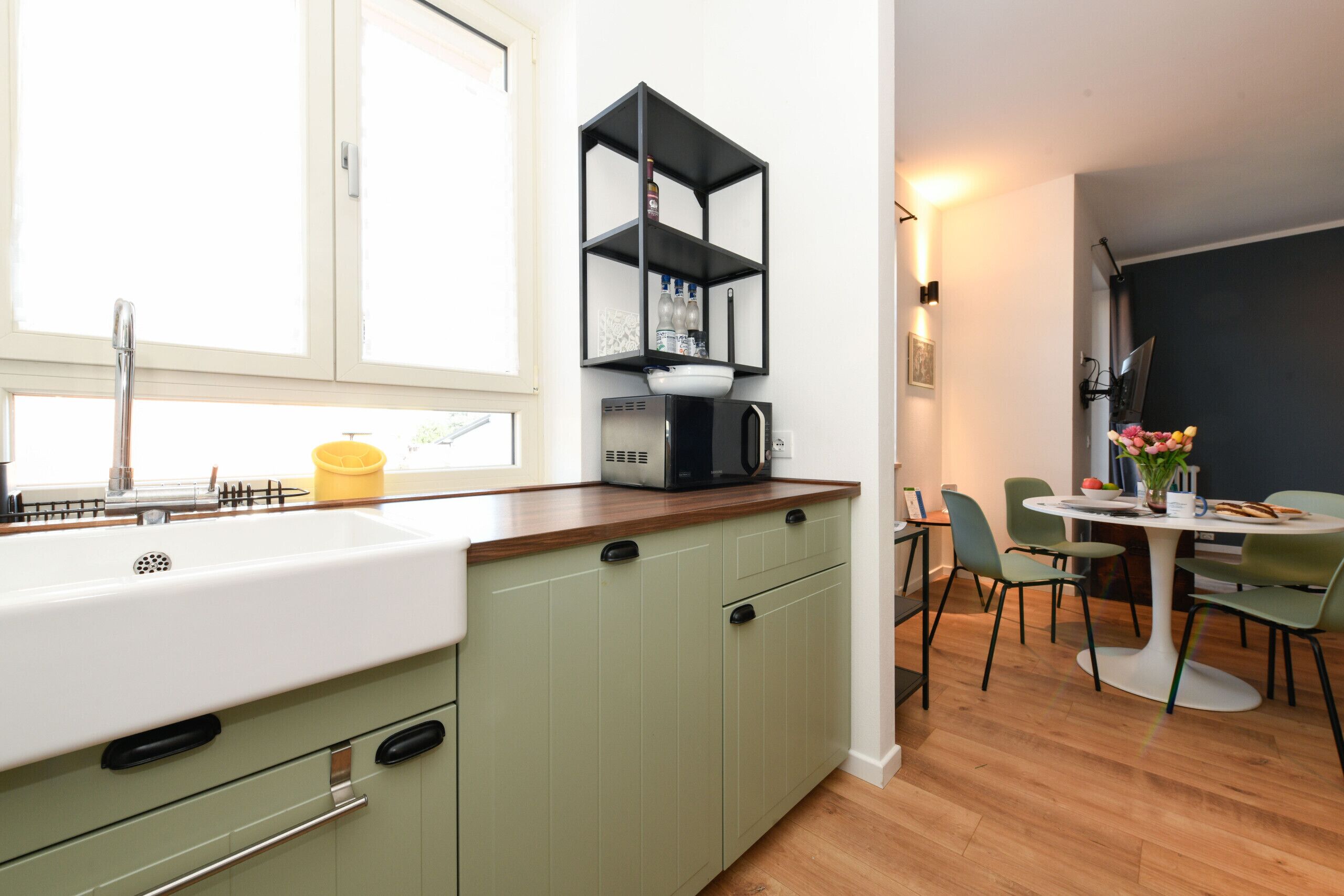 Une cuisine compacte équipée d’un évier, d’un four à micro-ondes et d’une étagère noire. On y trouve également un coin repas avec une table ronde et des chaises.