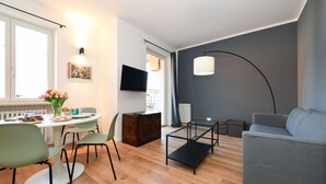 Ein modernes Wohnzimmer mit einem grauen Sofa, einem Esstisch mit Stühlen und einem an der Wand befestigten Fernseher.