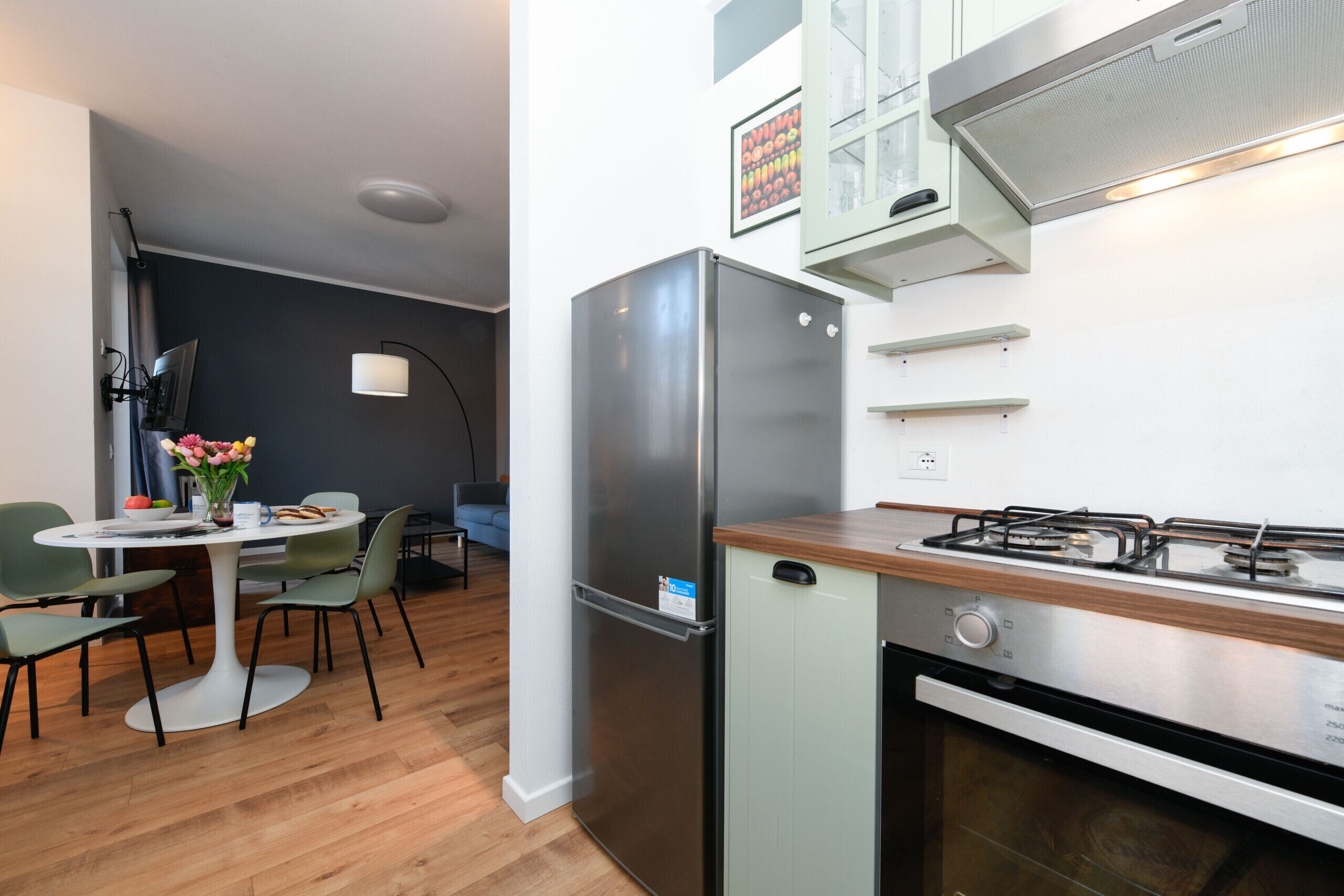 Una cocina compacta con un refrigerador de acero inoxidable, un horno empotrado y una estufa a gas.