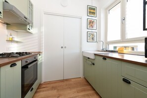 A compact kitchen with a gas stove, oven, and a sink. There are framed pictures on the wall and a window providing natural light. - Garden Apartment Bardolino - Petrol Apartment (Bardolino)