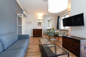 A modern living room with a sofa, a glass coffee table, a wooden cabinet, and a flat-screen TV mounted on the wall. - Garden Apartment Bardolino - Petrol Apartment (Bardolino)