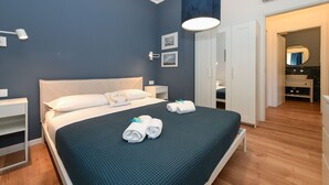 Ein modernes Hotelzimmer mit einem großen Bett, Nachttischen, einem Kleiderschrank und einem durch eine offene Tür einsehbarer Badezimmer.