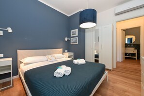 A modern hotel room with a large bed, bedside tables, a wardrobe, and a bathroom visible through an open door. - Garden Apartment Bardolino - Petrol Apartment (Bardolino)