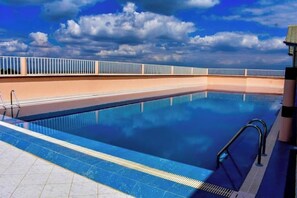 Une piscine à l’eau d’un bleu limpide, avec une terrasse carrelée et une rambarde.