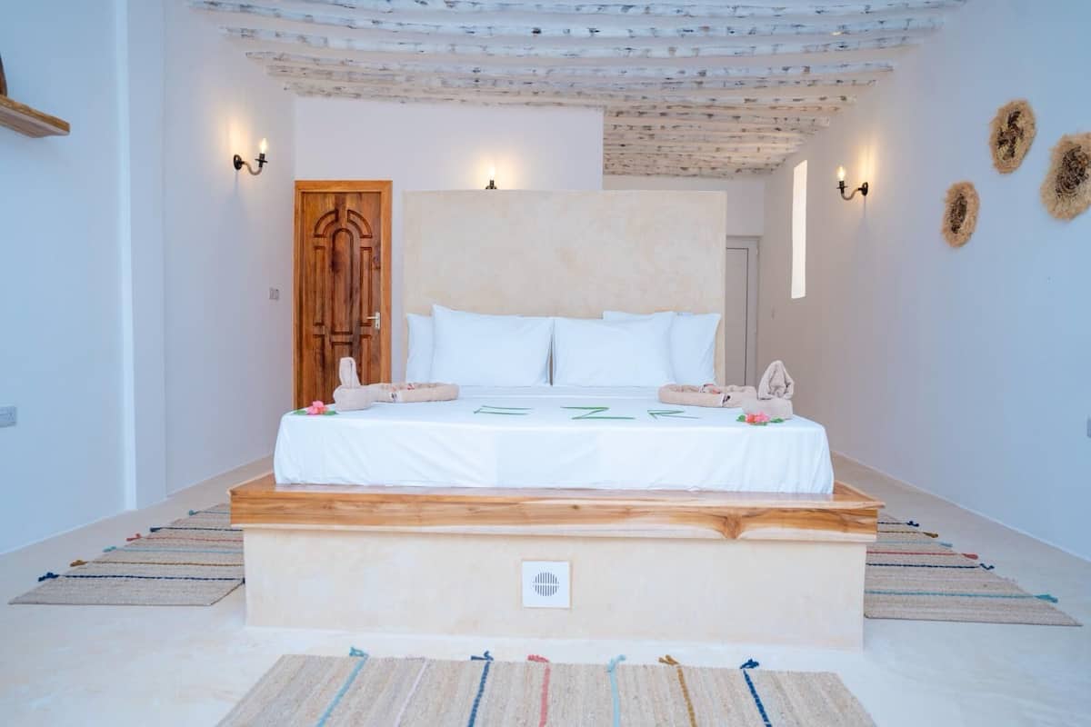 Quarto com cabeceira de madeira, roupa de cama branca e pequena mesa de cabeceira com abajur.