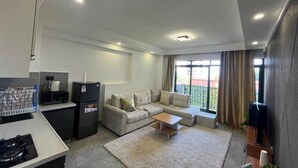 A modern living room with a sofa, coffee table, and a kitchen area with a refrigerator and microwave. - Nairobi Accomodation (Nairobi)