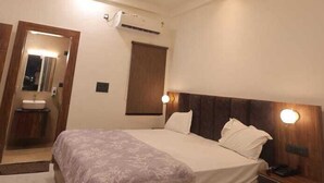 A modern bedroom with a wooden bed, bedside tables, a nightstand, a ceiling fan, and an air conditioning unit. - Priya Kunj Dham (Mathura)