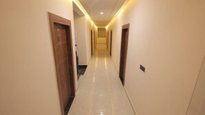 A hotel hallway with a polished floor, wooden doors, and recessed lighting. - Priya Kunj Dham (Mathura)