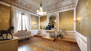 A room with ornate ceiling, a chandelier, a desk, a sofa, and a horse statue. - Hotel Palazzo Borghini (Florence)