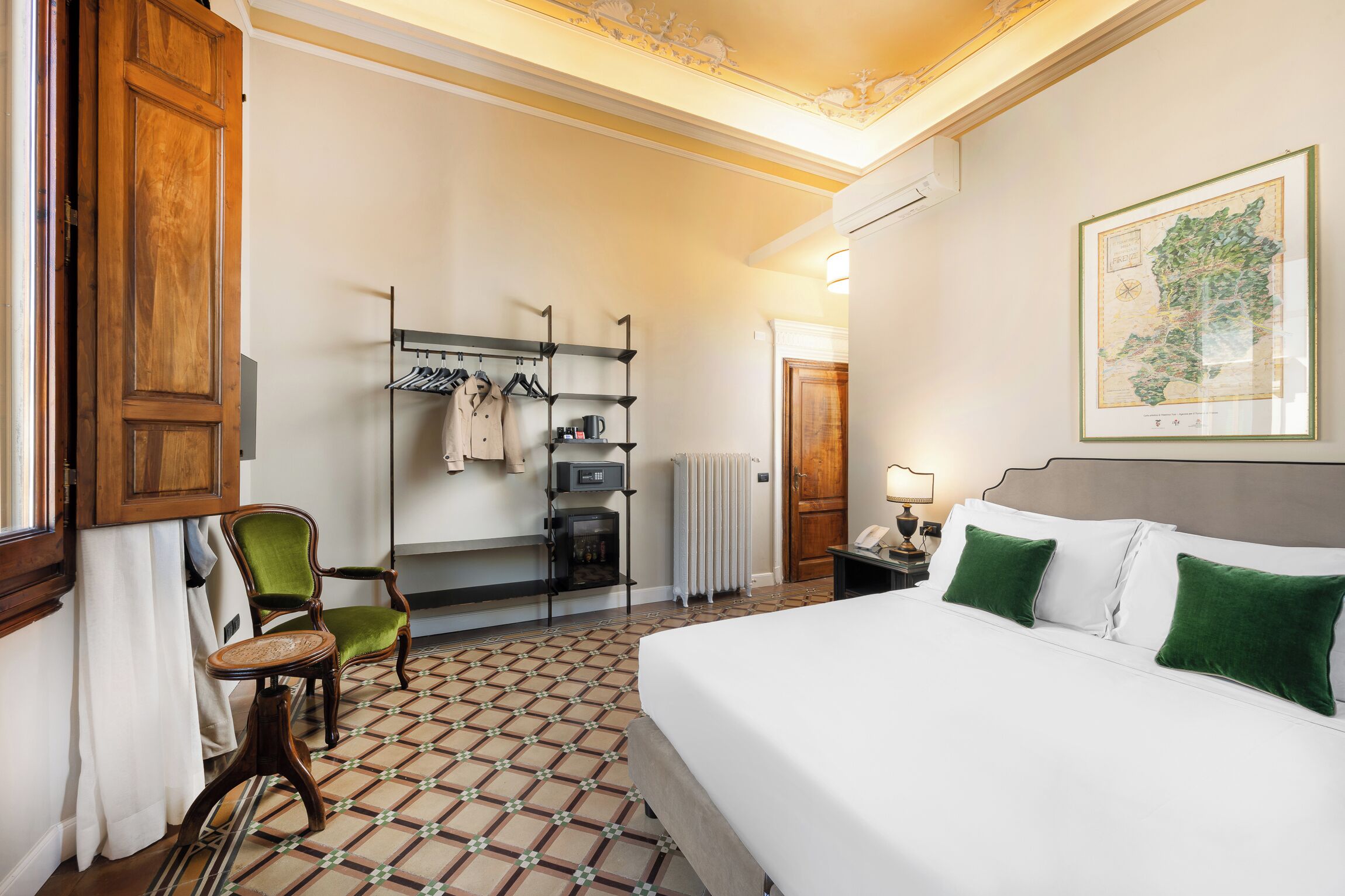 Une chambre d’hôtel avec un lit, une chaise, un bureau avec une bouilloire, un radiateur et une carte accrochée au mur.