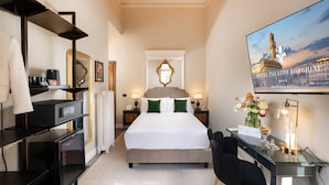 A hotel room with a bed, desk, chair, TV, and a painting of a building. - Hotel Palazzo Borghini (Florence)