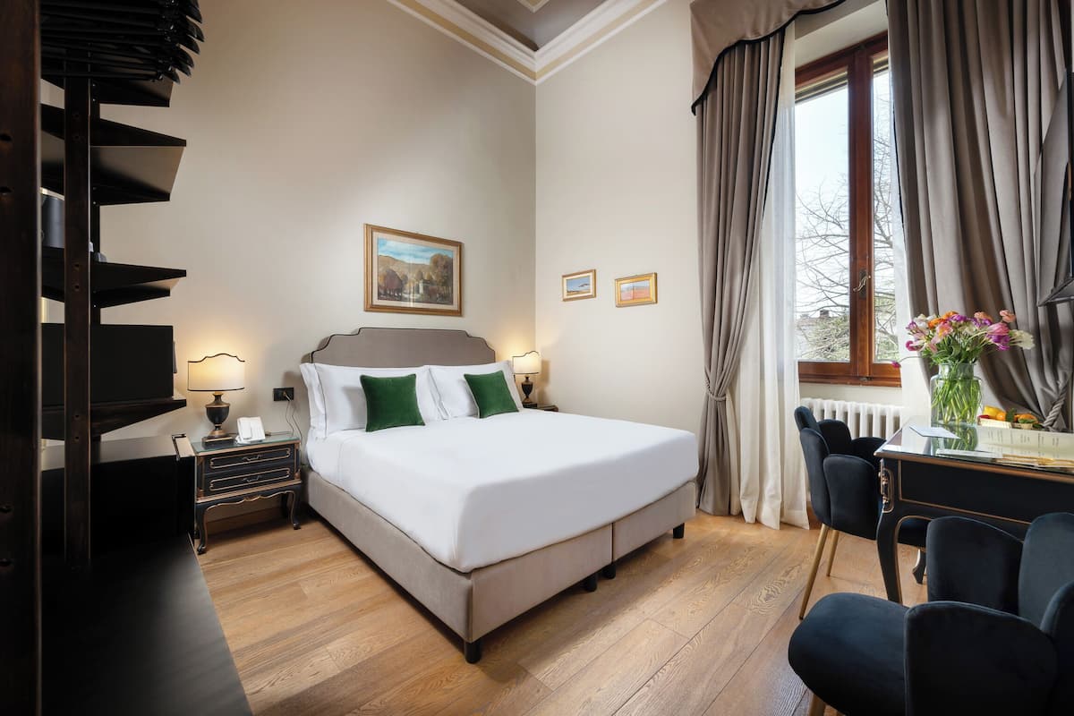 Ein Hotelzimmer mit Bett, Nachttischen, einem Schreibtisch und einem Fenster mit Vorhängen.