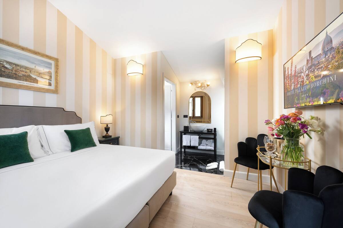 Ein Hotelzimmer mit Bett, einer Sitzecke mit Tisch und Stühlen, einem Spiegel und einem gerahmten Bild an der Wand.