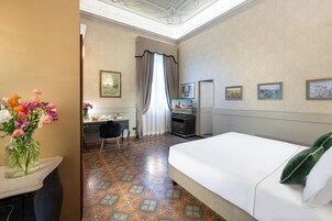 Una camera d'albergo con un letto, una scrivania, una sedia, un vaso di fiori e vista sulla città dalla finestra.