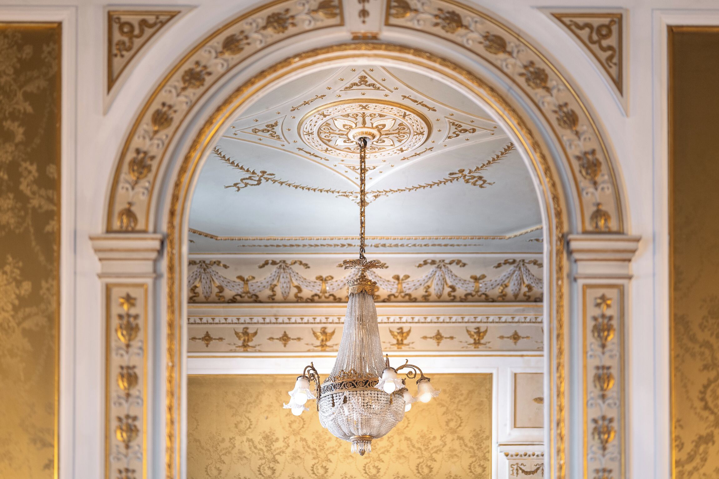 A chandelier with multiple lights hanging from a ceiling with ornate gold detailing.