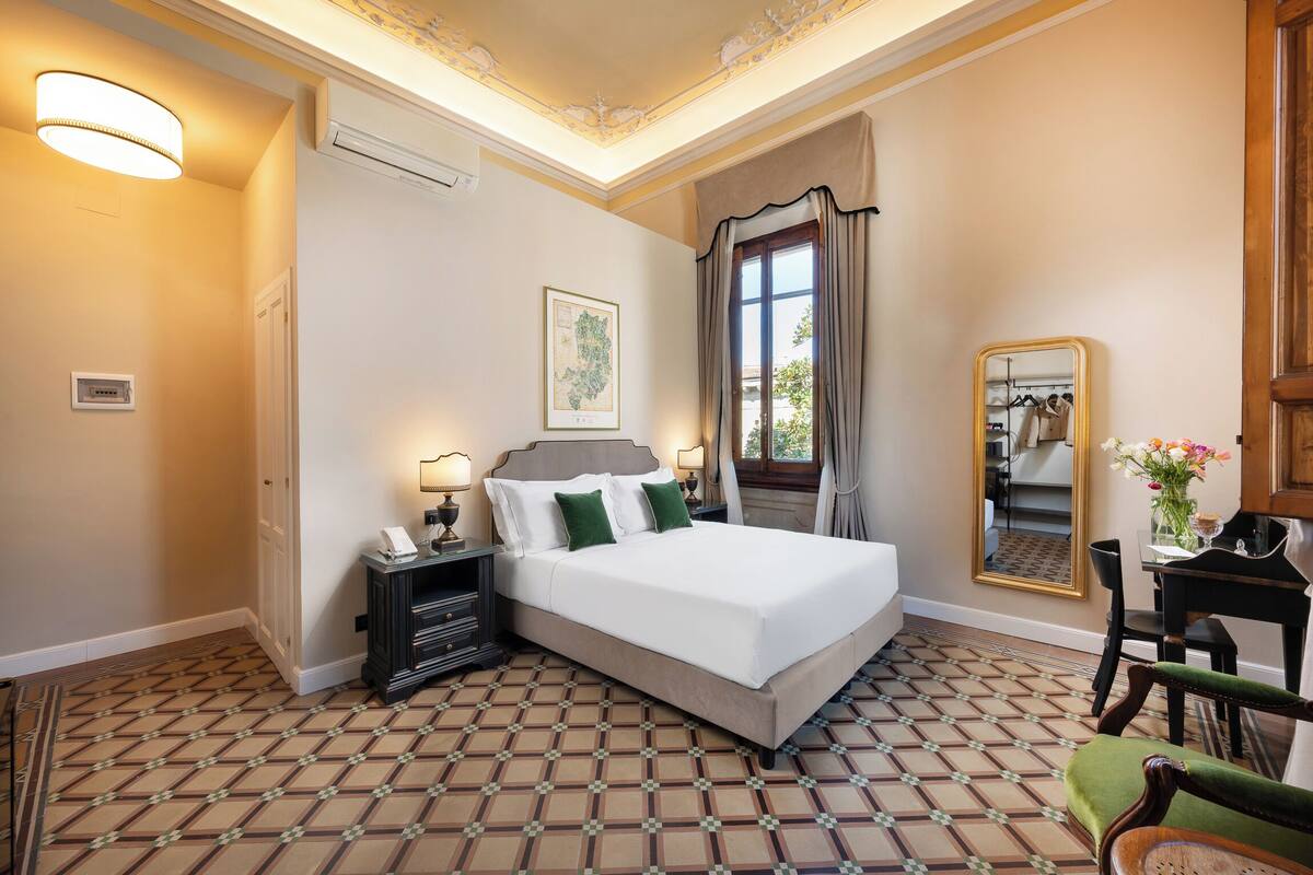 Ein Hotelzimmer mit Bett, Nachttischen, einem Spiegel, einem Sessel und einem gemusterten Boden.