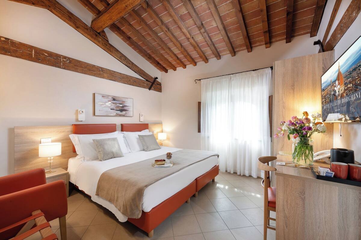 Ein Hotelzimmer mit Bett, Schreibtisch, Stuhl, Nachttisch und einem Fenster mit Vorhängen.
