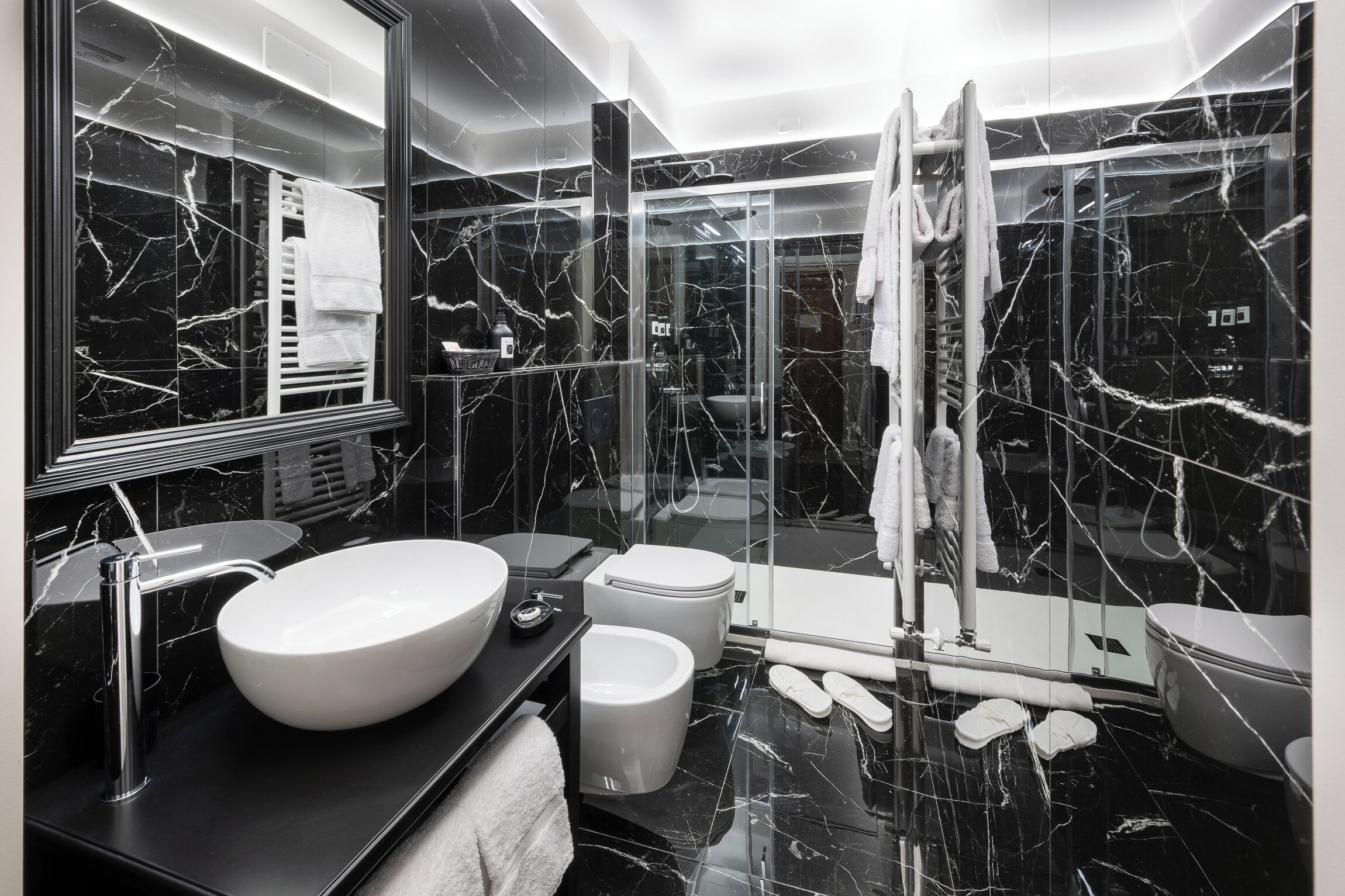 A modern bathroom with a large white sink, a glass shower enclosure, and a marble-tiled floor.
