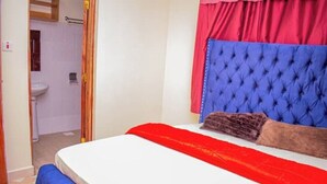 A bedroom with a bed, a red and blue headboard, and a red bedspread. - Dandy Home, 2 BdRm, Estn Bypass Kamakis Greenspot (Ruiru)