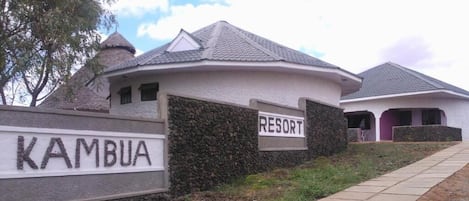 A resort named KAMBUA with a stone wall entrance and a paved pathway leading to the buildings.