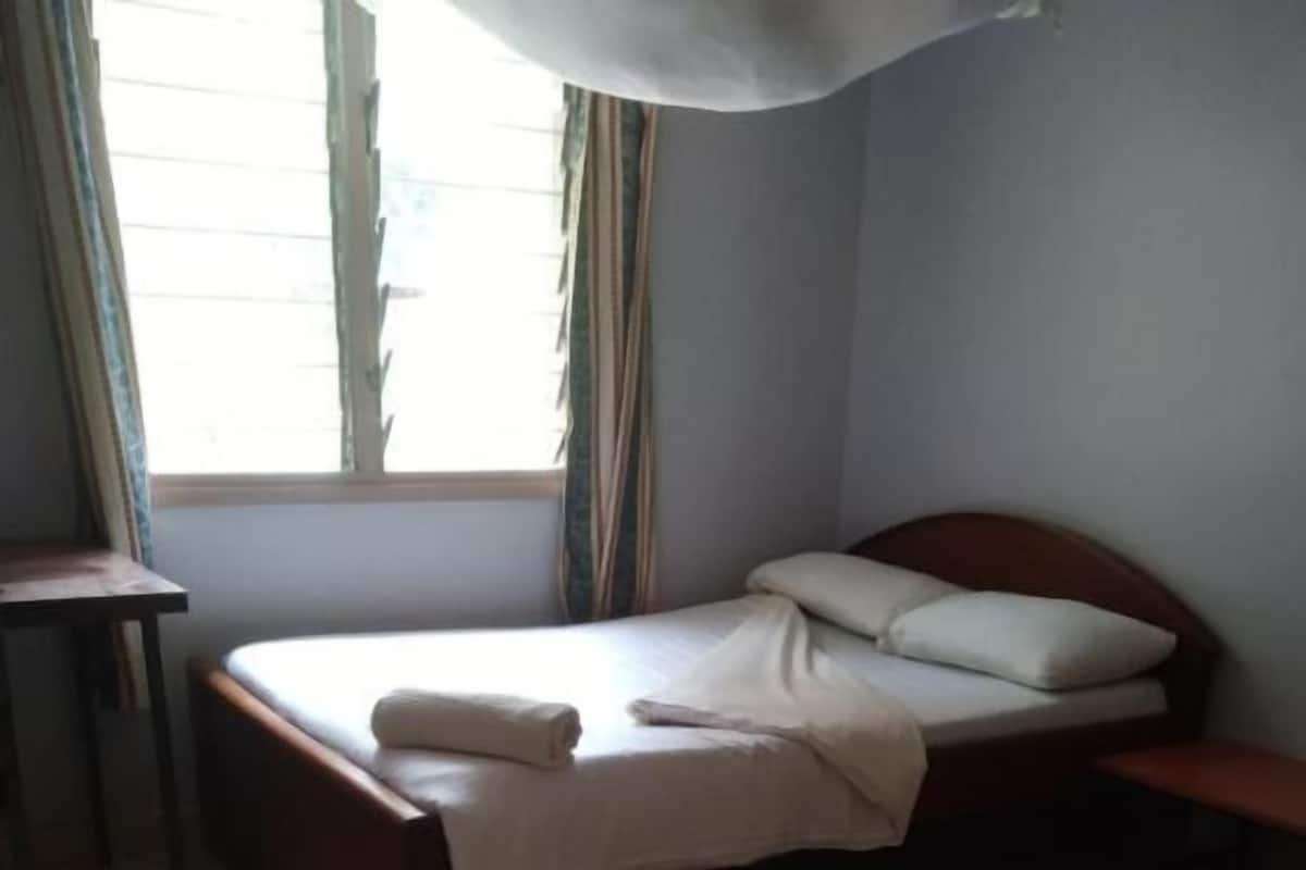 Ein Zimmer mit einem Bett, einem kleinen Tisch und einem fensterbepflanzten Fenster.