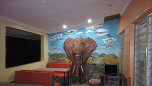 En restaurant med et vægmaleri af en elefant, røde og blå siddepladser, og et tv-skærm.