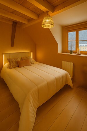 A bedroom with a large bed, a window with a view, a radiator, and a hanging light fixture. - Cauterets City Center, apartment for 4–6 people, renovated in 2025 (Cauterets)
