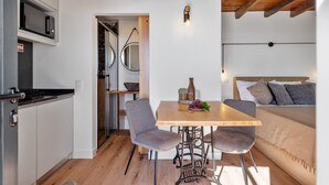 A compact kitchen with a microwave, a dining table with chairs, and a bed with pillows. - Authentic Madeira stay • Ocean View Apartments (Caniço)