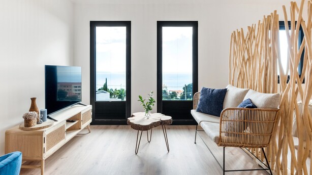 A modern living room with a TV, sofa, and a view through large windows. - Authentic Madeira stay • Ocean View Apartments (Caniço)