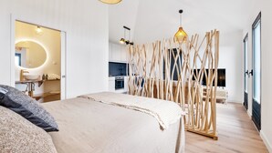 A modern bedroom with a large bed, a bedside mirror, a wooden partition, and a kitchen area in the background. - Authentic Madeira stay • Ocean View Apartments (Caniço)