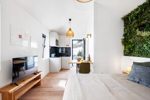 A modern room with a bed, a TV on a wooden stand, a small kitchen, and a green wall. - Authentic Madeira stay • Ocean View Apartments (Caniço)