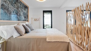 Ein Schlafzimmer mit einem Bett, einem großen abstrakten Gemälde, einer gewobenen Leuchte, einer Holzwand und Blick durch eine Tür.