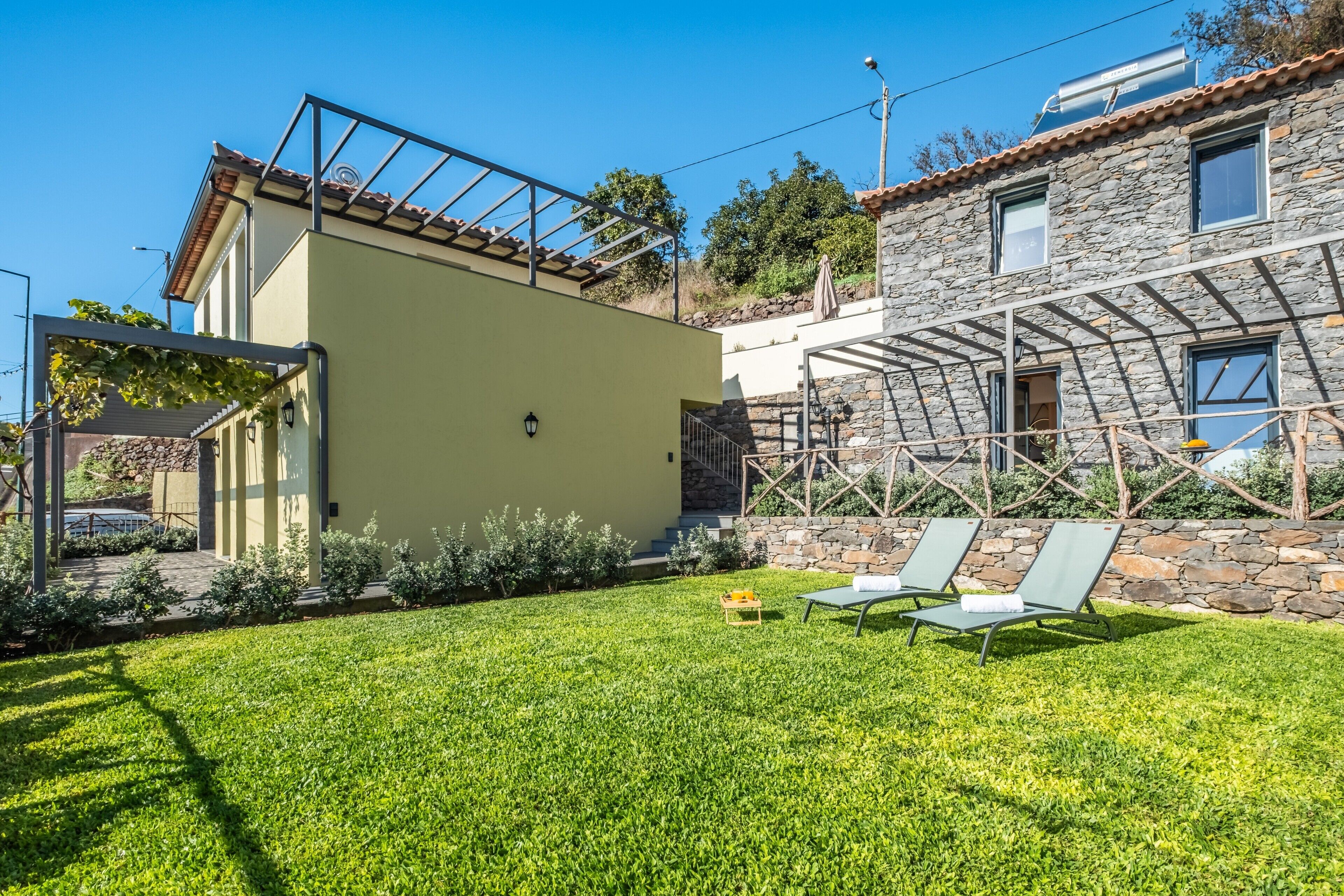 A house with a stone facade, a green lawn, and two lounge chairs.