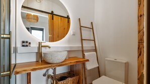 A bathroom with a round mirror, wooden vanity, white sink, and a white toilet. - Studio Apartment 'Ocean View Rock House  2' with Balcony and Wi-Fi (Caniço)