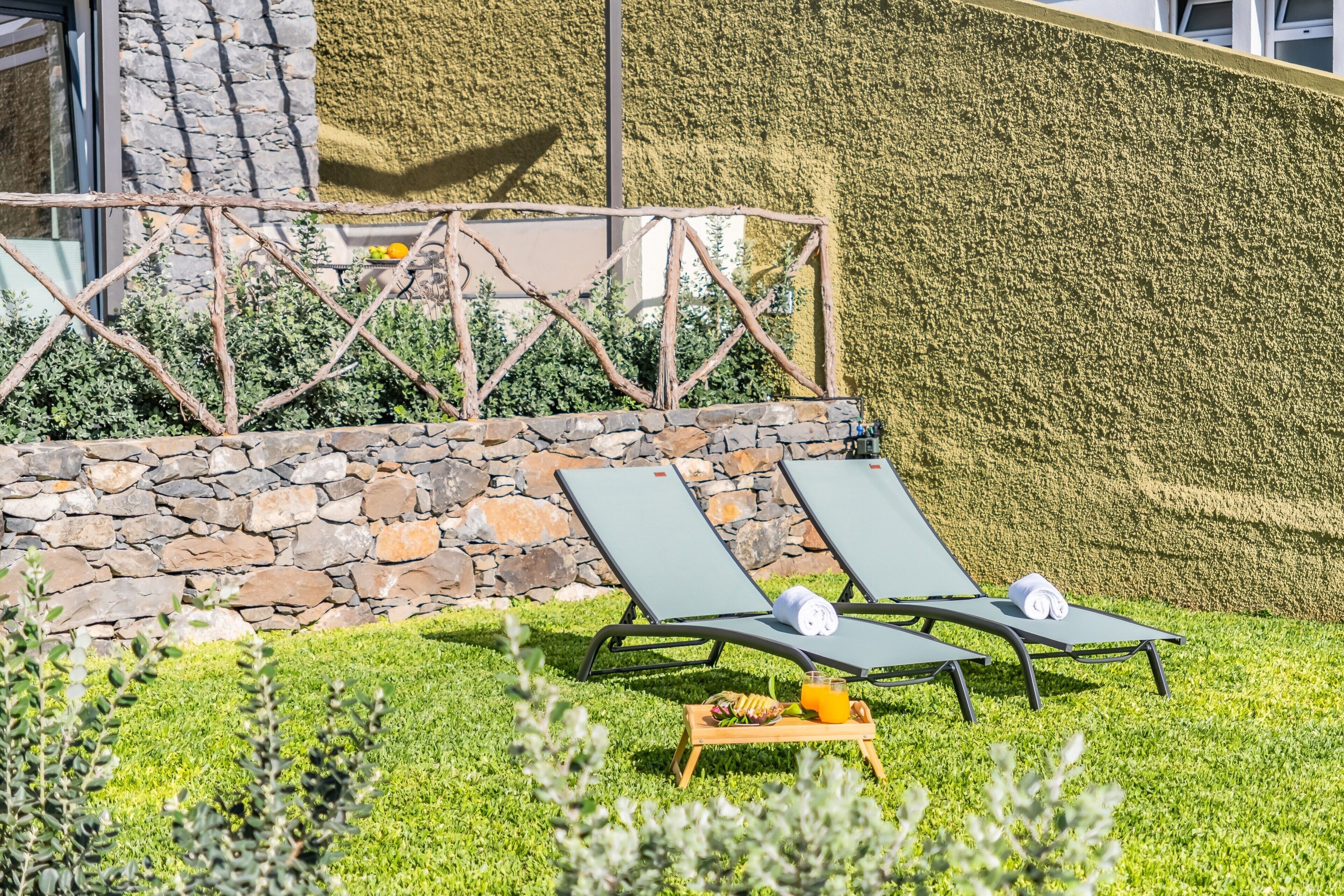 A terrace with two lounge chairs, a stone wall, and a green wall with a textured surface.