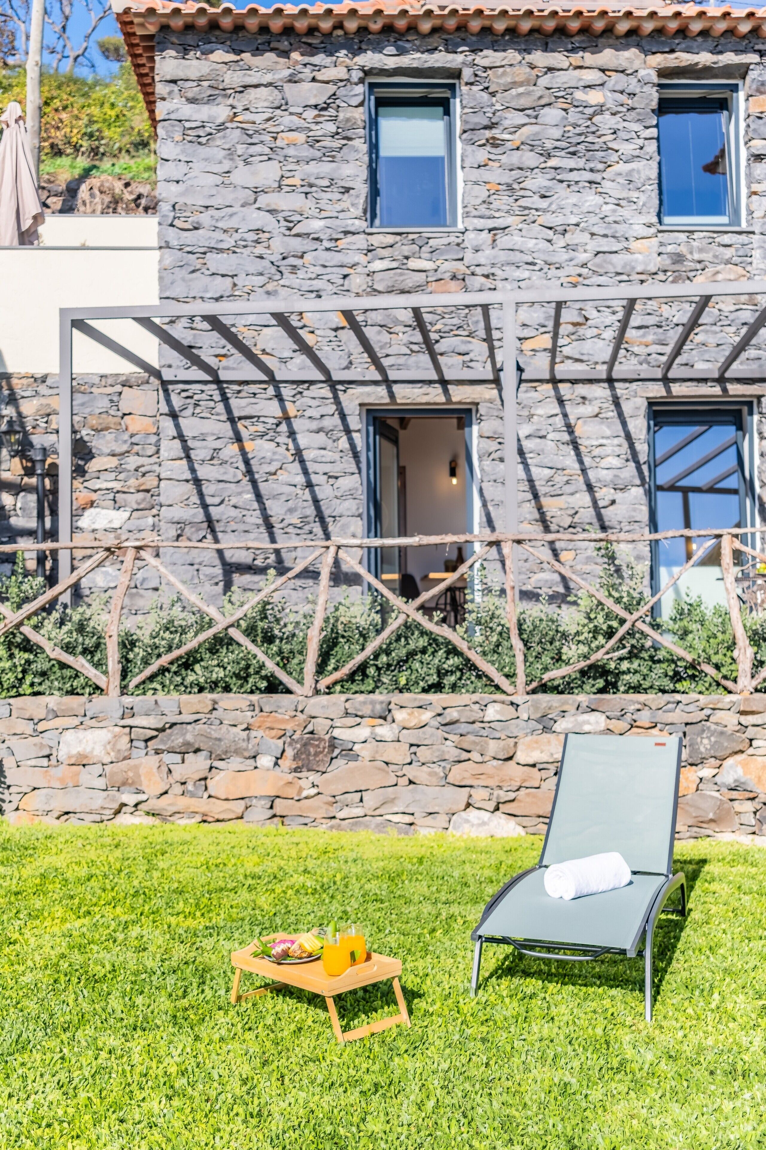 A stone building with a balcony, a lounge chair, and a table with a tray.