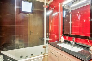 Une salle de bain avec une douche à parois de verre, une baignoire blanche, un lavabo avec un miroir et des murs recouverts de carreaux rouges.