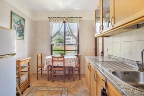 A kitchen with a dining table, chairs, a refrigerator, and a window with curtains.