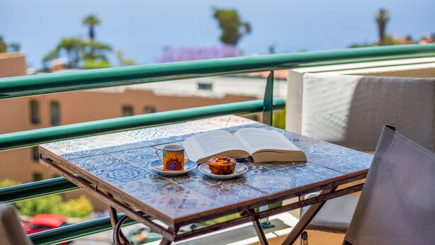 A balcony with a table set for a meal, a book, and a cup. - Sunny Ocean View Apartment • Pool & Open Horizon (Caniço)