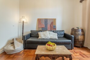 A living room with a sofa, a coffee table with fruit, a lamp, a wall art piece, and a barrel. - Above Funchal · A Hillside Home with Ocean Views (Funchal)