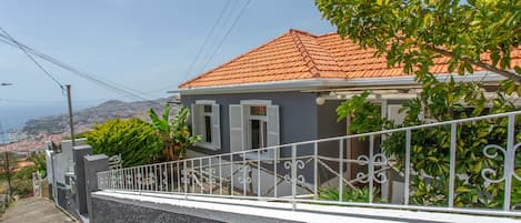 A residential building with a red-tiled roof, white shutters, and a balcony with a metal railing.
