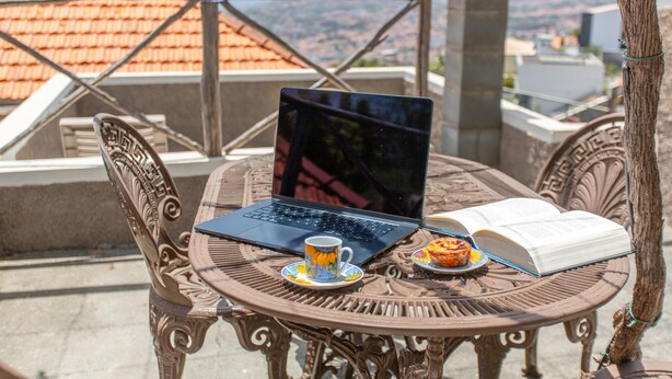Een laptop op een tafel, met een open boek en een muffin op een schoteltje.