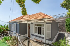 A house with a red-tiled roof, white shutters, and a small porch area. - Above Funchal · A Hillside Home with Ocean Views (Funchal)