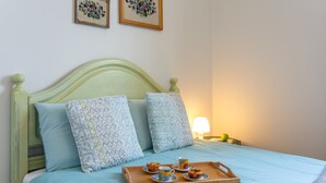 Een bed met een houten hoofdbord, twee kussens met dessin, een dienblad met een mok en gebak, en een lamp op een nachtkastje.