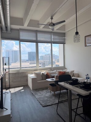 A modern living room with a sofa, dining table, and city view through large windows. - Cozy 1-bedroom apartment with AC in beautiful Atlanta (Atlanta)