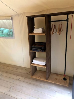 Una tenda amb una estanteria de fusta que conté tovalloles doblades i un penjador amb roba.