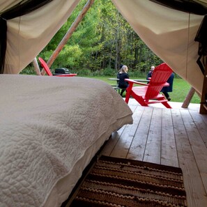A tented accommodation with a bed, red chairs, and a picnic table.