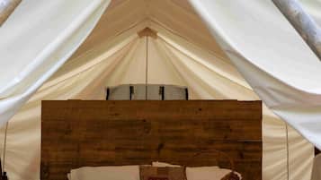 A tent with a wooden headboard, white bedding, and two red chairs.