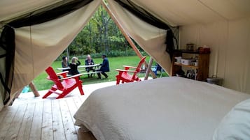 A tent with a bed, red chairs, and a table outside.